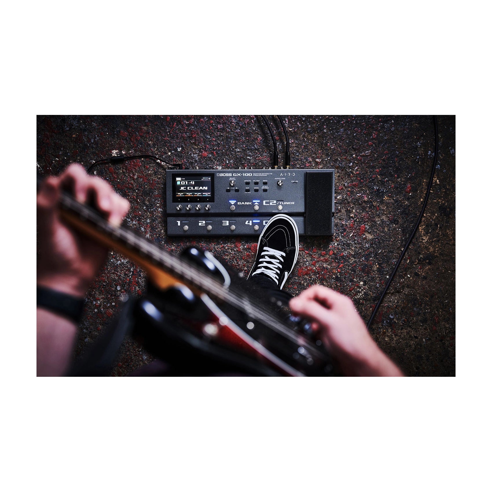 Guitarist playing electric guitar with effects pedal on a textured surface