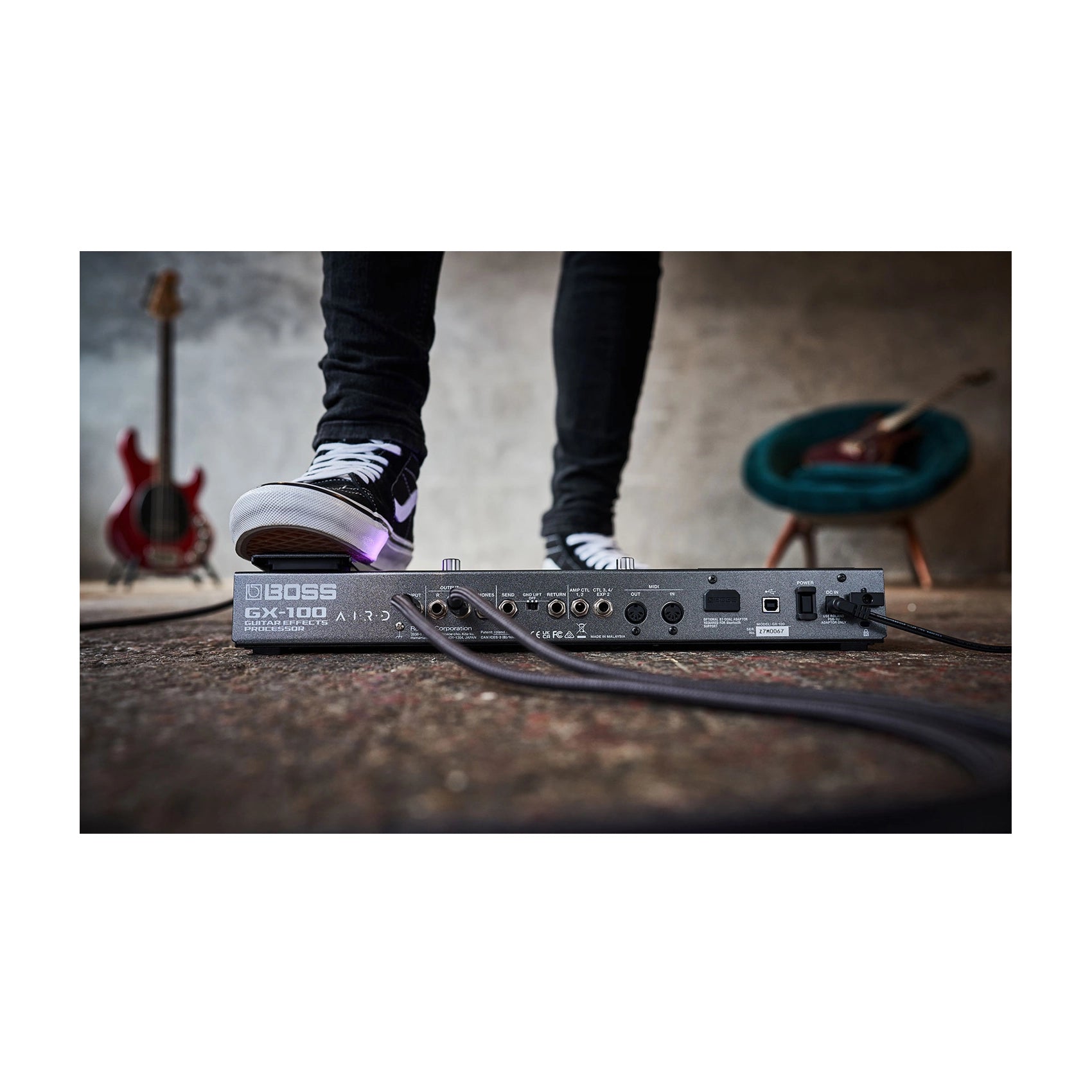 Boss guitar effects pedal on a wooden floor with a blurred background of a person and guitars.