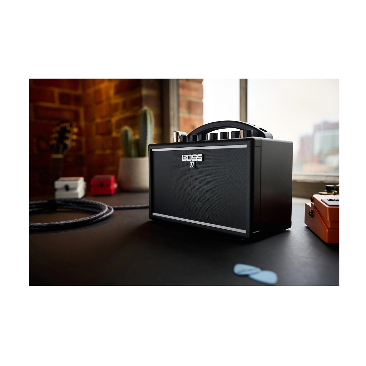 Boss Katana 7W Mini Guitar Amp on a desk with guitar pedals and headphones