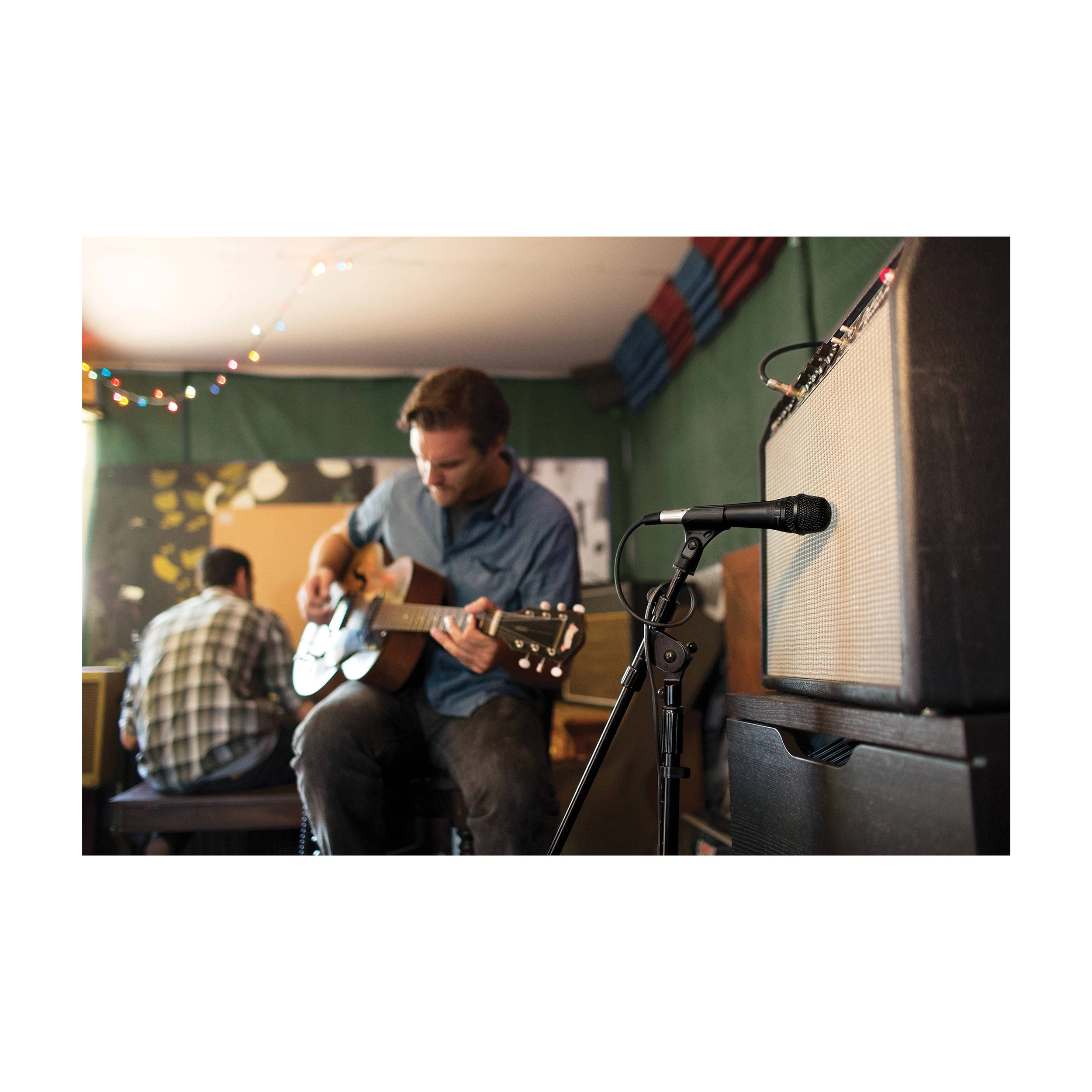 Man playing guitar in a room with a microphone and amplifier.