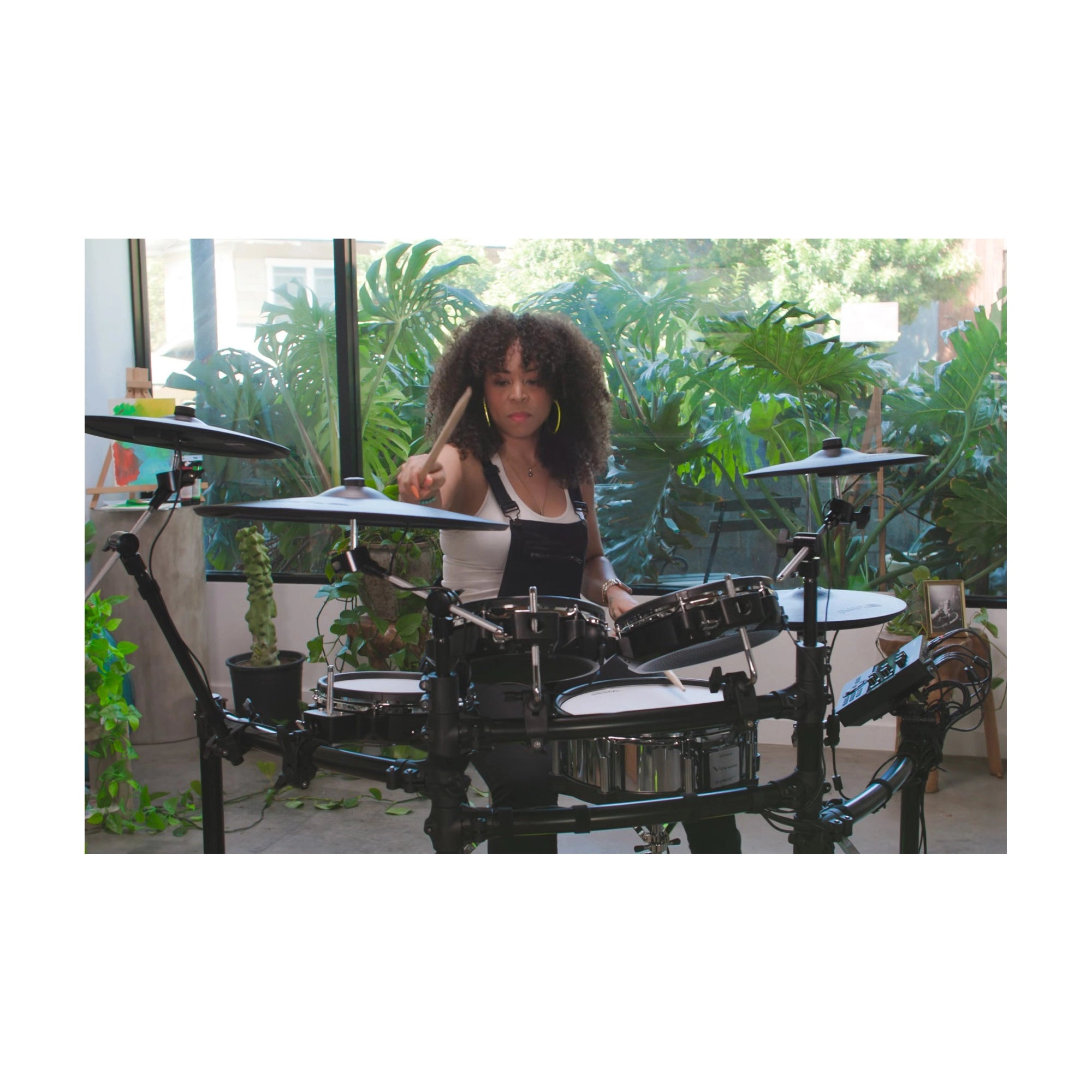 Person playing a set of electronic drums in a room with plants